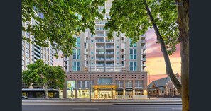 Experience the sleek, modern architecture of this urban hotel, featuring a symmetrical facade with balconies and commercial establishments at its base.