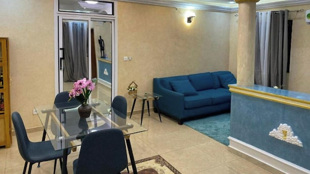 Un salon avec un canapé bleu, une table à manger en verre entourée de chaises et un vase décoratif rempli de fleurs.