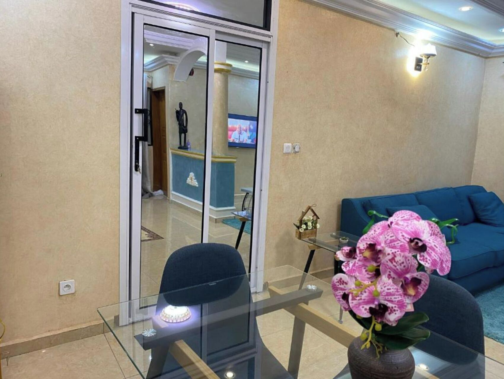 Een moderne woonkamer met een glazen tafel, een blauwe bank en een roze orchidee.