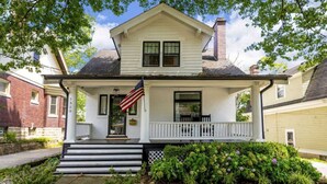 Una casa a due piani con un portico, un'entrata e una bandiera americana.