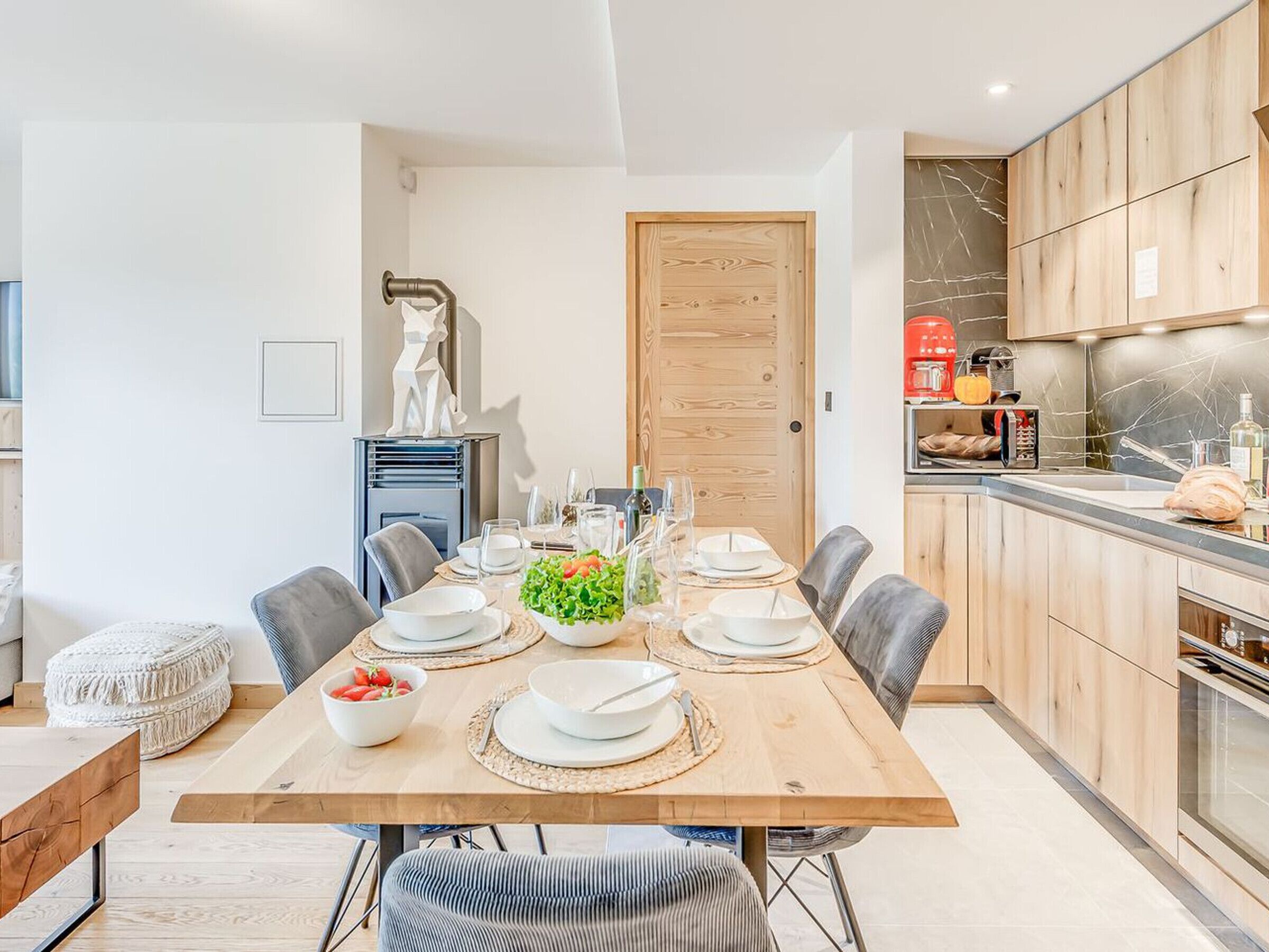 Une cuisine moderne avec des meubles en bois, un four encastré et un coin repas doté d’une table en bois, mise pour six personnes.