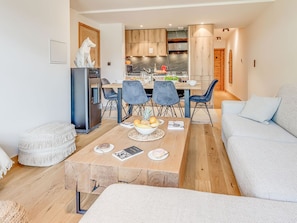 Una sala de estar moderna con una mesa de centro de madera, un sofá y una zona de comedor con una cocina al fondo.
