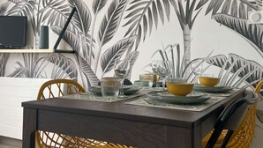 A dining area with a modern table, chairs, and a decorative wall with a leaf pattern. - Appt Centre de Courseulles - 100m de la Plage (Courseulles-sur-Mer)