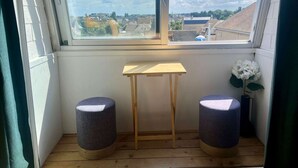 A room with a large window, a small wooden table, two round stools, and a potted white flower. - Appt Centre de Courseulles - 100m de la Plage (Courseulles-sur-Mer)