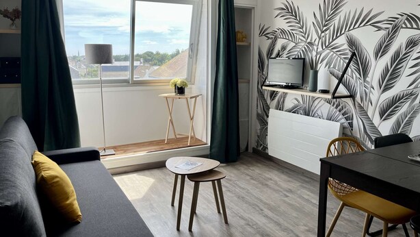 A modern living room with a grey sofa, a small round table, a dining table with chairs, and a TV on a shelf. - Appt Centre de Courseulles - 100m de la Plage (Courseulles-sur-Mer)