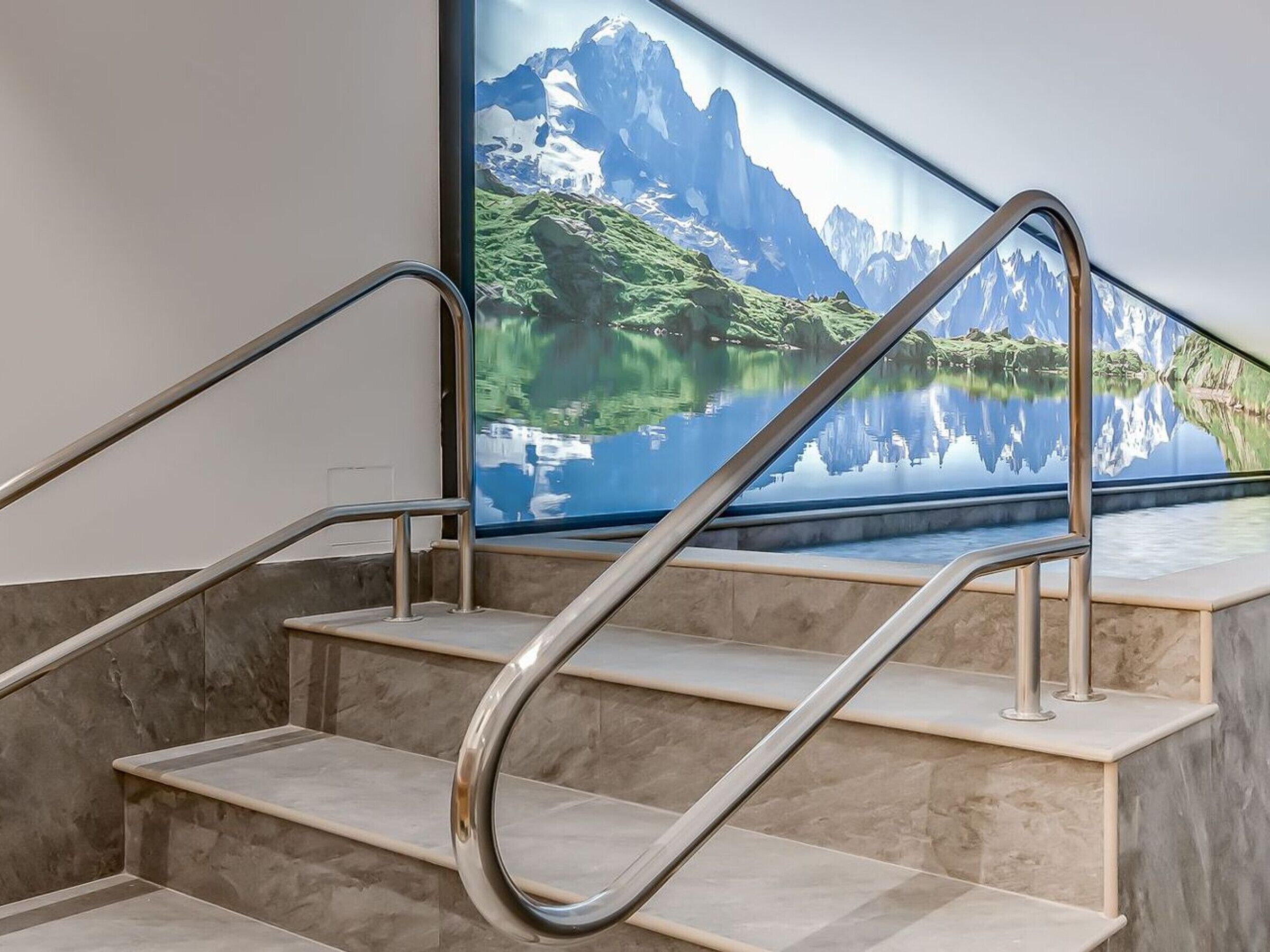 A set of marble stairs with metal handrails, leading to a large window with a scenic mountain and lake view.
