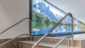 A set of marble stairs with metal handrails, leading to a large window with a scenic mountain and lake view.