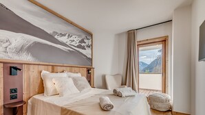 A bedroom with a bed, a chair, a large window, and a painting of mountains.