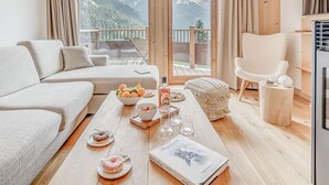 A modern living room with a sofa, a coffee table with snacks and drinks, and a view of mountains through large glass doors. - Champagny en Vanoise: Apartment 6 people, 3 rooms, balcony (Champagny-en-Vanoise)