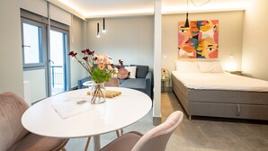Une chambre d’hôtel moderne avec un lit, une table à manger avec des chaises, un vase de fleurs et une grande fenêtre.