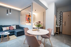 A modern living room with a grey sofa, a round table with chairs, and a painting on the wall.