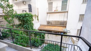 Un balcon doté d’une rambarde en métal, donnant sur une cour intérieure agrémentée de verdure et sur un immeuble comportant de nombreux balcons.