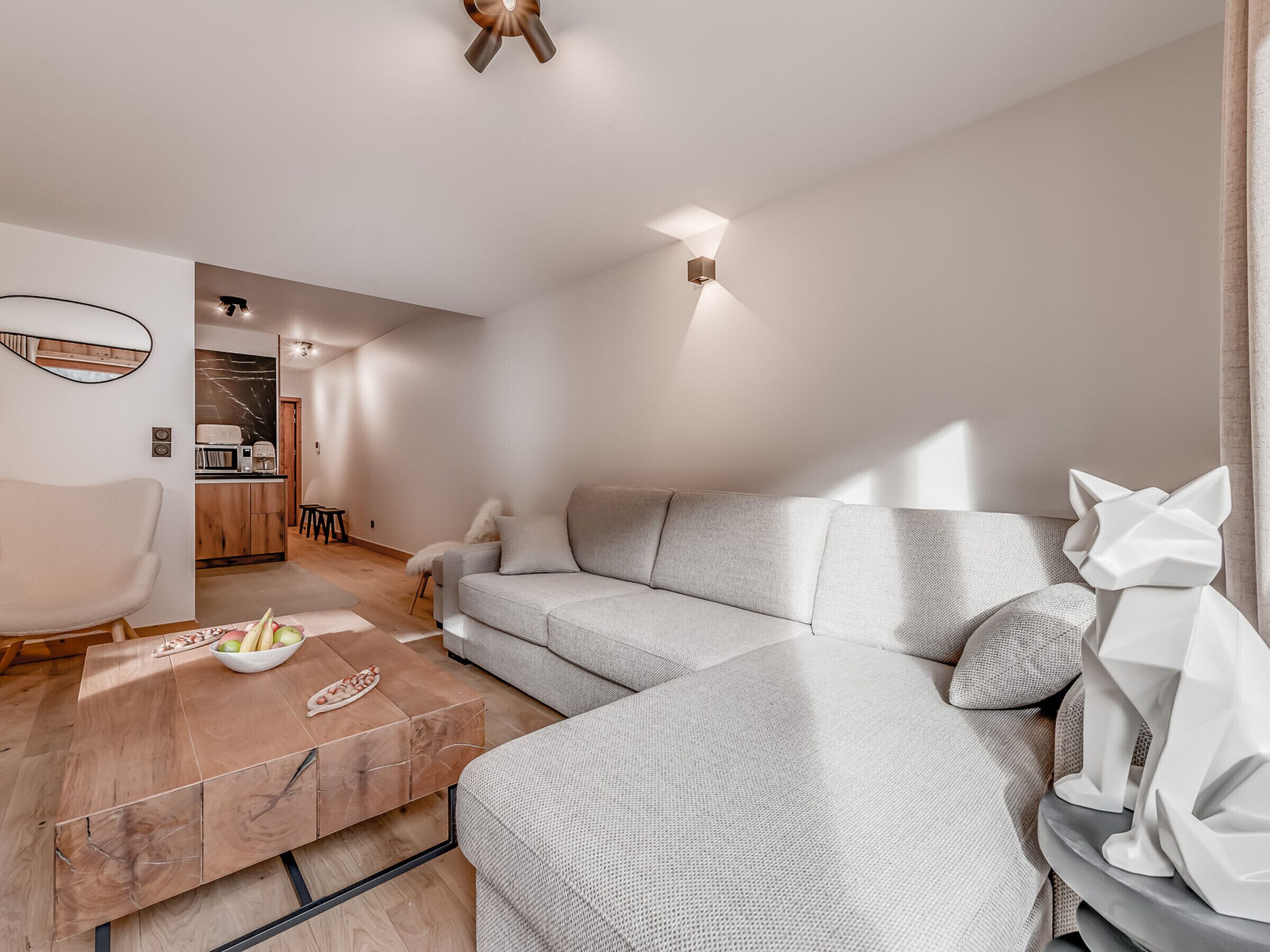Una sala de estar moderna con un sofá seccional gris, una mesa de centro de madera con frutas, y una decoración minimalista que incluye una escultura de gato.