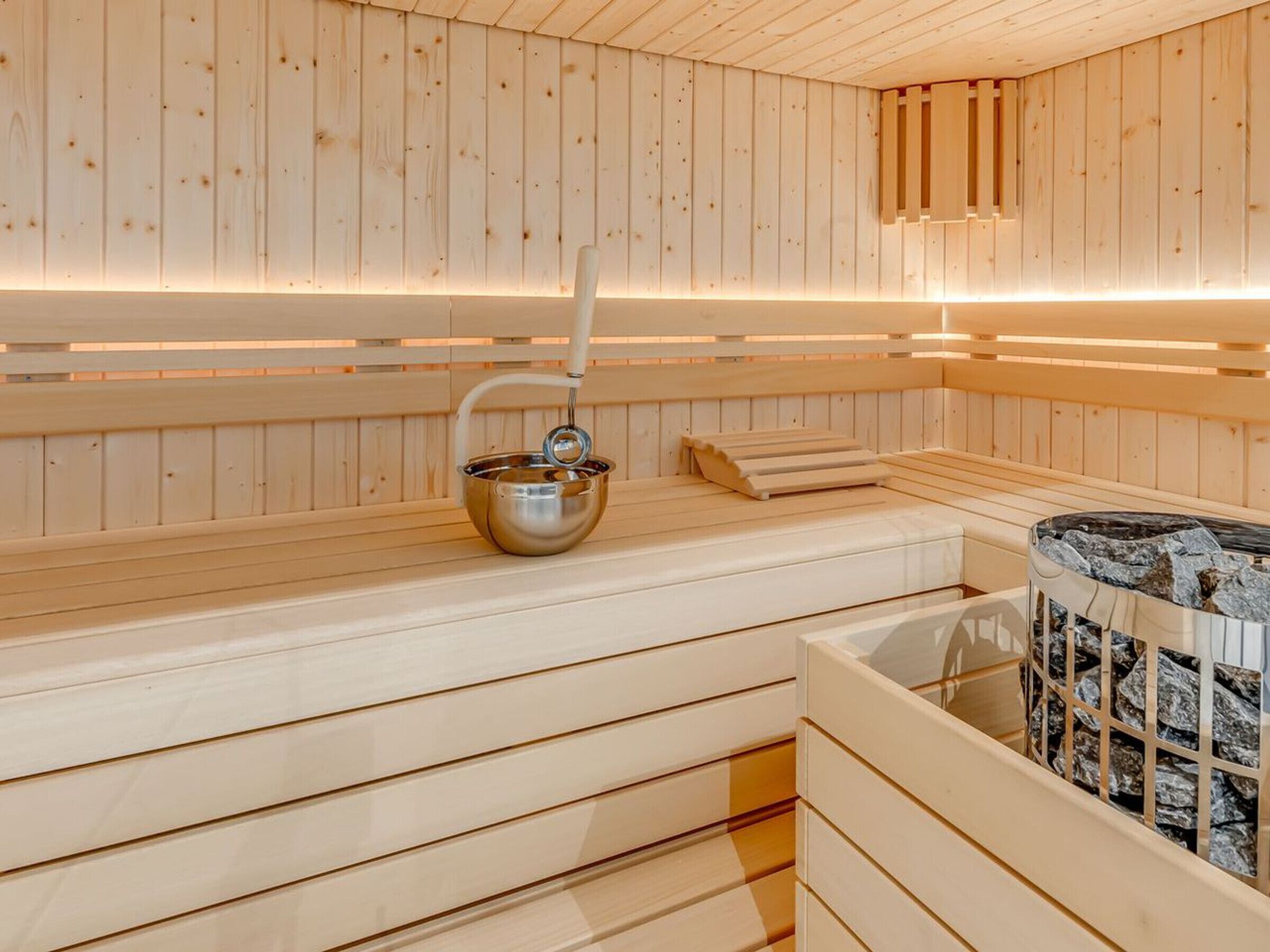 A sauna with wooden walls and benches, a metal basin, and a stone heating element.
