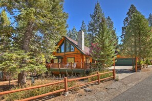 A log cabin with a stone chimney, surrounded by tall trees and a wooden fence.