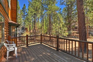 A wooden deck with a railing, surrounded by tall pine trees.