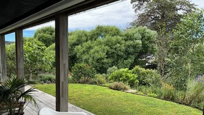A covered outdoor area with a wooden deck, potted plants, and a view of a well-maintained garden with various shrubs and trees.