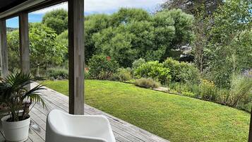 A covered outdoor area with a wooden deck, potted plants, and a view of a well-maintained garden with various shrubs and trees.