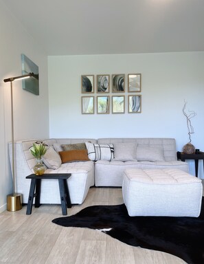 Ein modernes Wohnzimmer mit einem Ecksofa, einem schwarz-weißen Teppich, einer Stehlampe und abstrakter Wandkunst.