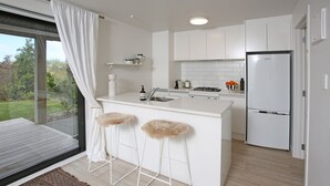 Una cocina moderna con armarios blancos, una isla integrada con taburetes, un refrigerador y vistas al exterior.