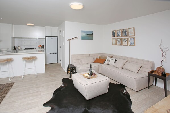 A modern living room with a sofa, ottoman, and a black leather rug. - Garden apartment Self-contained luxury just 5 mins walk to Village!  (Matakana)