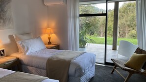 Habitación de hotel con cama, mesita de noche, lámpara y vistas al exterior a través de una puerta corrediza de vidrio.