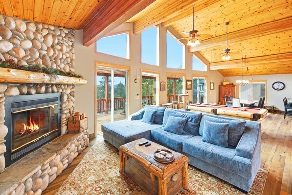 A spacious living room with a stone fireplace, a blue sofa, and a billiards table.