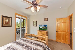 A bedroom with a bed, a ceiling fan, a television, and a wooden door. - Luxury! Stunning Views! Minutes from Bear Mountain! Air Conditioning! PET FRIENDLY! HOT TUB ! EV Charger! Pool Table! Foosball! Video Arcade Game! (Big Bear Lake)