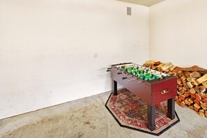 Una habitación con una mesa de fútbol de mesa, un tapete estampado y una pila de leña.