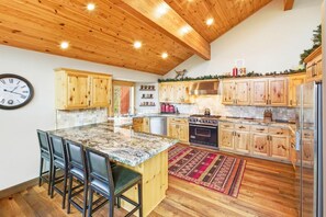 A kitchen with wooden cabinets, a central island with bar stools, a clock on the wall, and a stove.