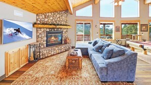 Una sala de estar acogedora con chimenea de piedra, un sofá grande y un televisor montado en la pared.