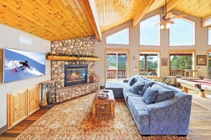 A cozy living room with a stone fireplace, a large sofa, and a television mounted on the wall.