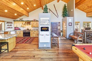 A spacious kitchen with wooden cabinets, a central island, and a pool table in a room with wooden floors and high ceilings. - Luxury! Stunning Views! Minutes from Bear Mountain! Air Conditioning! PET FRIENDLY! HOT TUB ! EV Charger! Pool Table! Foosball! Video Arcade Game! (Big Bear Lake)