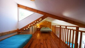 A bedroom with a sloped ceiling, wooden beams, a bed, a nightstand, and a window.