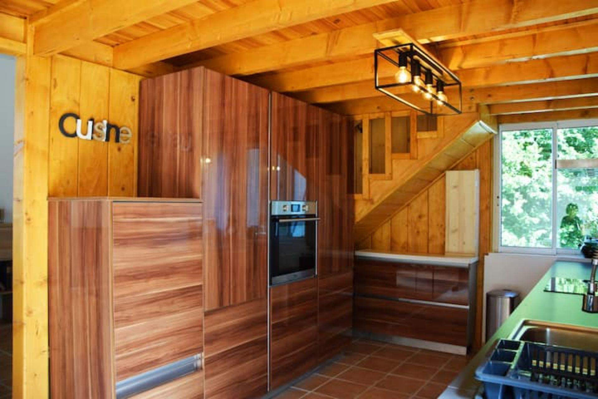 Een compacte keuken met houten kastjes, een inbouwoven en een trap naar een hoger gelegen verdieping.