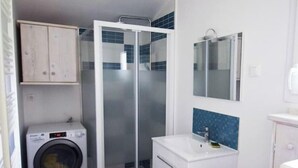 A compact bathroom with a washing machine, a glass shower enclosure, a sink, and a toilet.