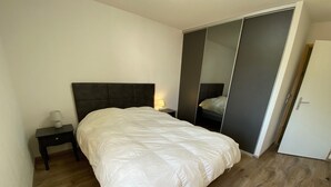 A bedroom with a bed, a nightstand, a bedside lamp, a wardrobe, and a door.