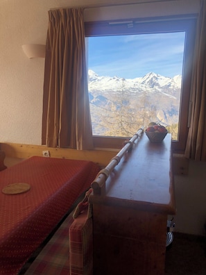 Ein Zimmer mit einem Bett, einem Holztisch und einem Fenster mit Blick auf die Berge.