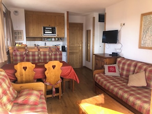 Ein gemütliches Wohnzimmer mit einer Couch, Sesseln, einem Fernseher und einer Küchenzeile mit Holdekor und einer Mikrowelle.