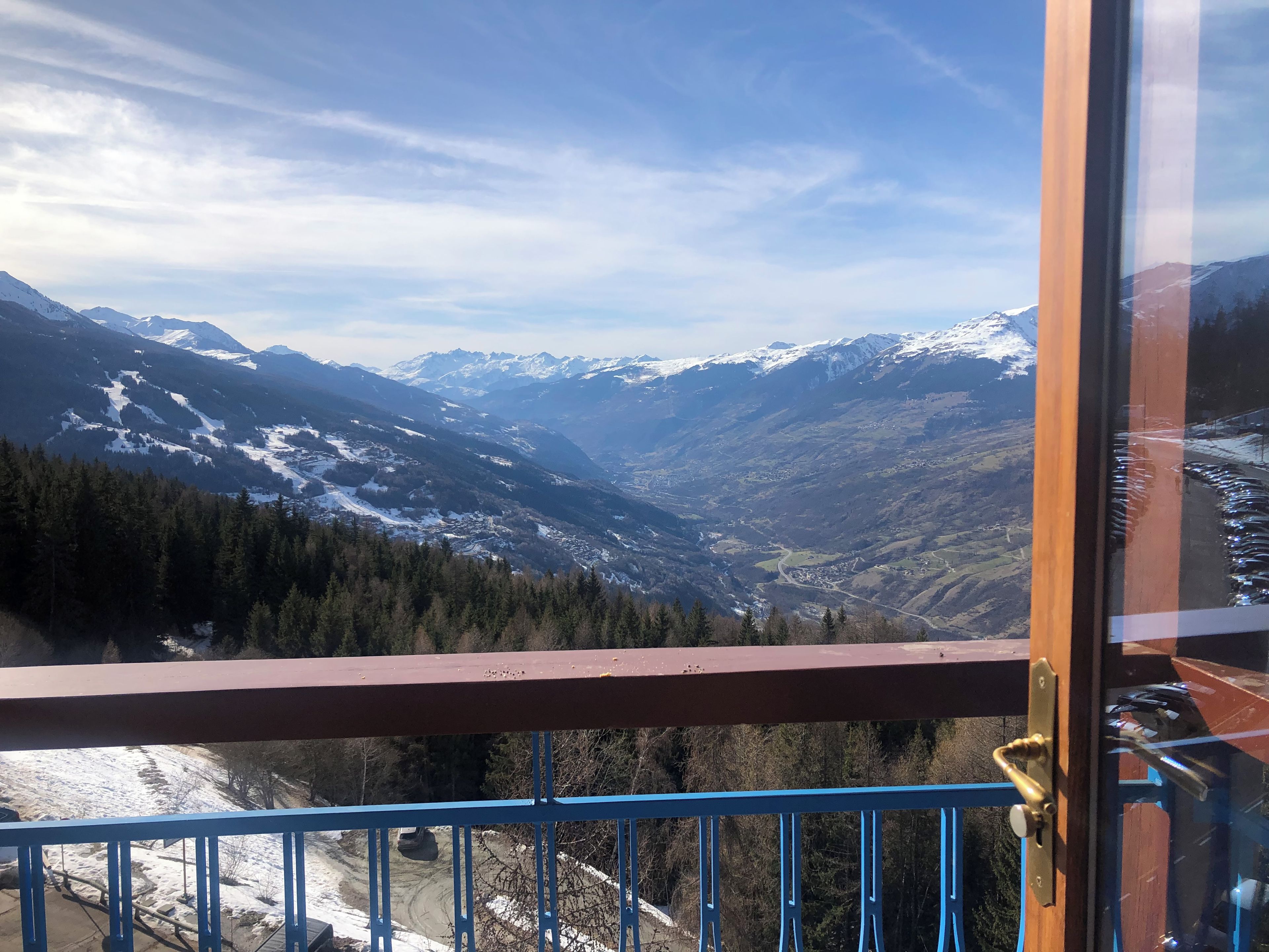 A balcony with a view of snow-covered mountains and a valley.