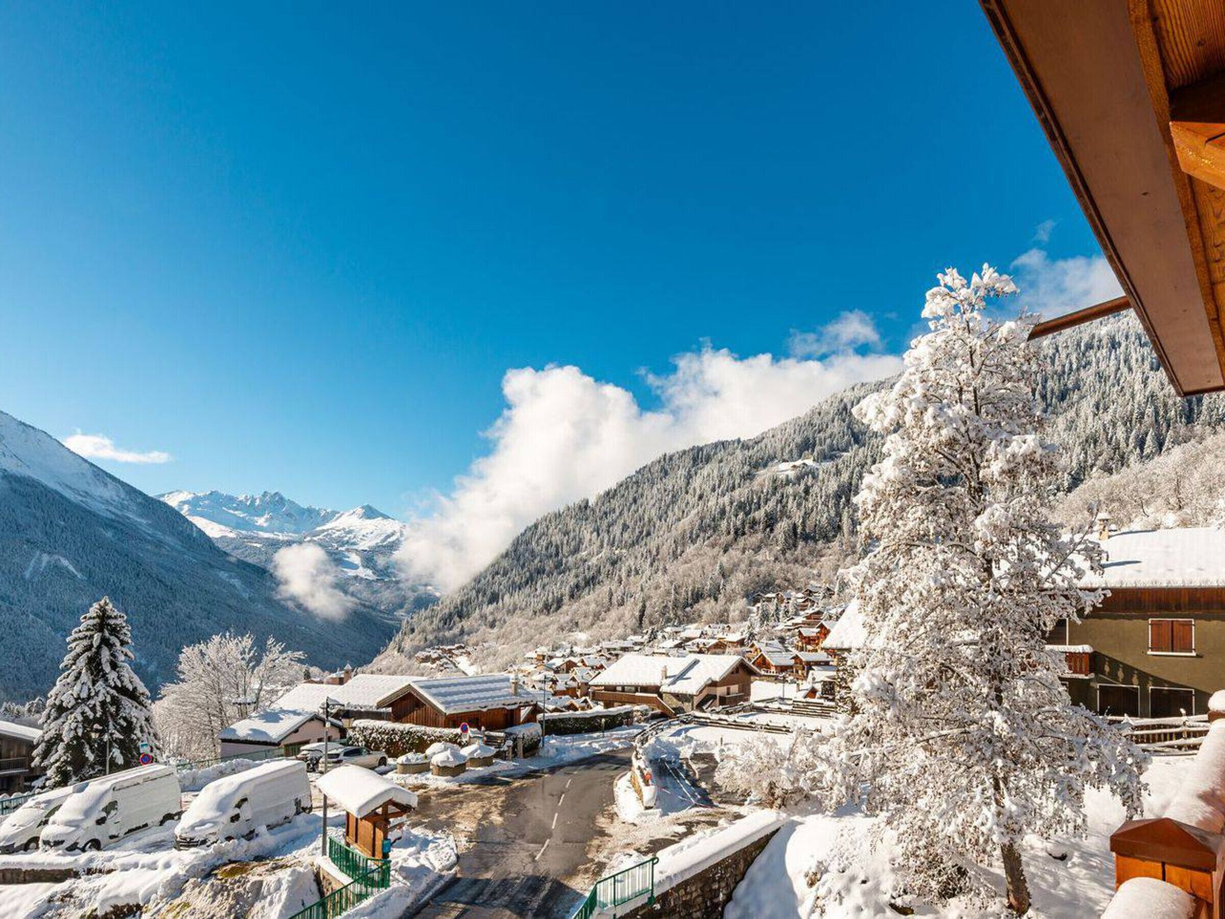 A snow-covered village with traditional wooden houses, a clear blue sky, and mountains in the background.