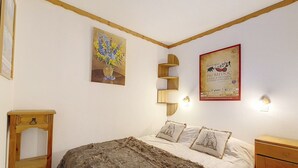 A bedroom with a large bed, a wooden nightstand, a small table, and a poster on the wall. - Comfy Apartment 4 pers. · Close to slopes · Balcony (Les Menuires)