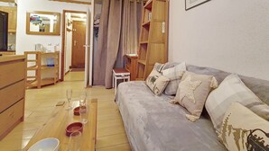 A cozy living room with a grey sofa, wooden side tables, and a dining area with a wooden table and chairs. - Comfy Apartment 4 pers. · Close to slopes · Balcony (Les Menuires)