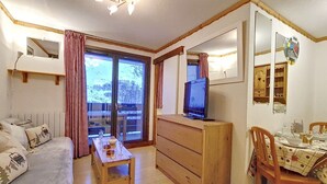 A cozy room with a bed, a wooden dresser, a television, and a dining table set for two. - Comfy Apartment 4 pers. · Close to slopes · Balcony (Les Menuires)
