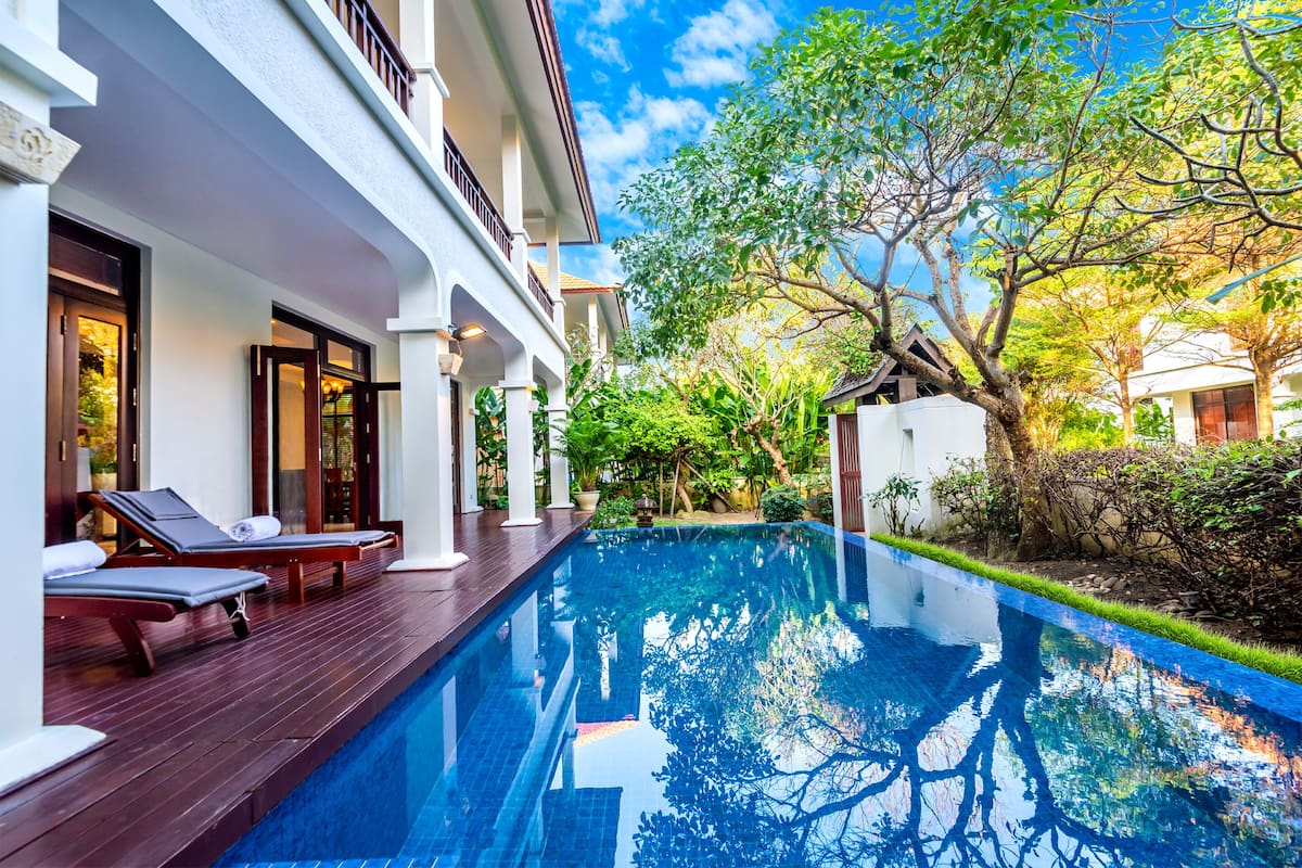 A swimming pool with lounge chairs and a white building with balconies.