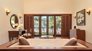 A hotel room with a large bed, a desk with a lamp, a chair, and a view of palm trees through the sliding doors. - Resort Villa Da Nang By Abogo (Da Nang)
