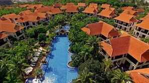 Un resort con varias edificaciones con techos de tejas rojas, una piscina central y abundante vegetación.
