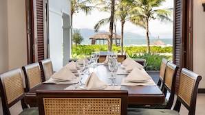 A dining table set for six with a view of the ocean and palm trees. - Resort Villa Da Nang By Abogo (Da Nang)