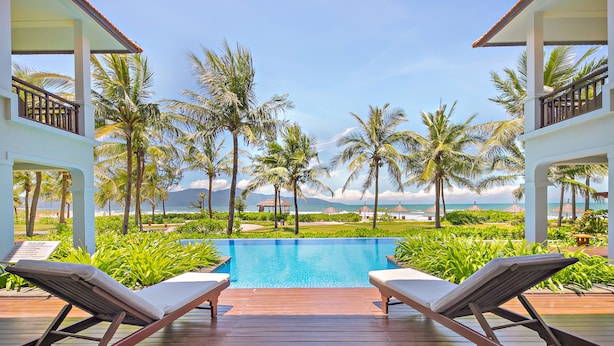 A poolside area with lounge chairs and a view of the ocean. - Resort Villa Da Nang By Abogo (Da Nang)
