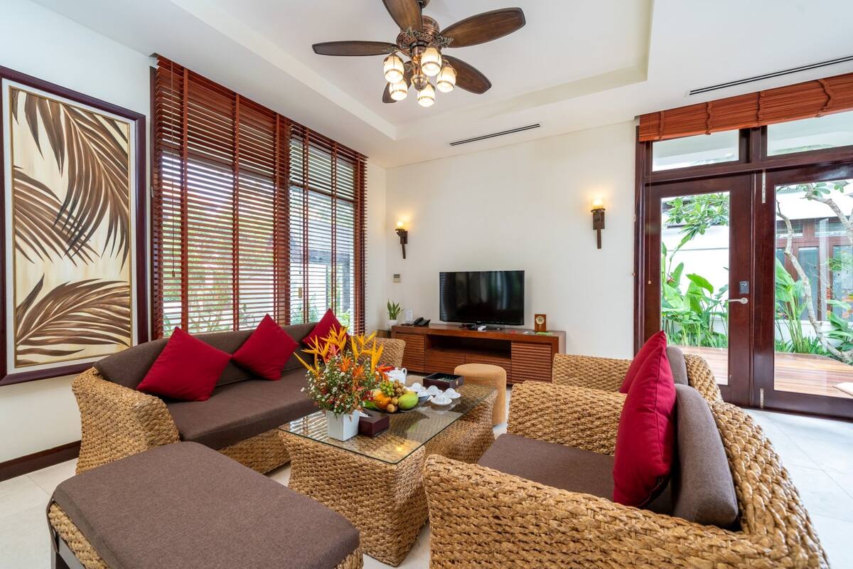 A living room with a sofa, coffee table, and wicker chairs. There is a television on a wooden cabinet and a ceiling fan.